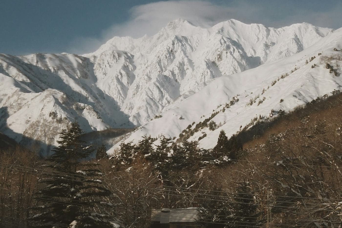 Snow-covered mountain peaks in morning light above snowy trees and a house in Hakuba