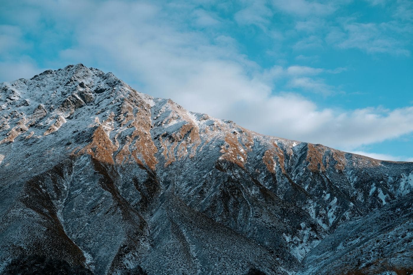 A rocky ridge dusted with fresh snow under a blue sky, seen from the Ben Lomond Track above Queenstown