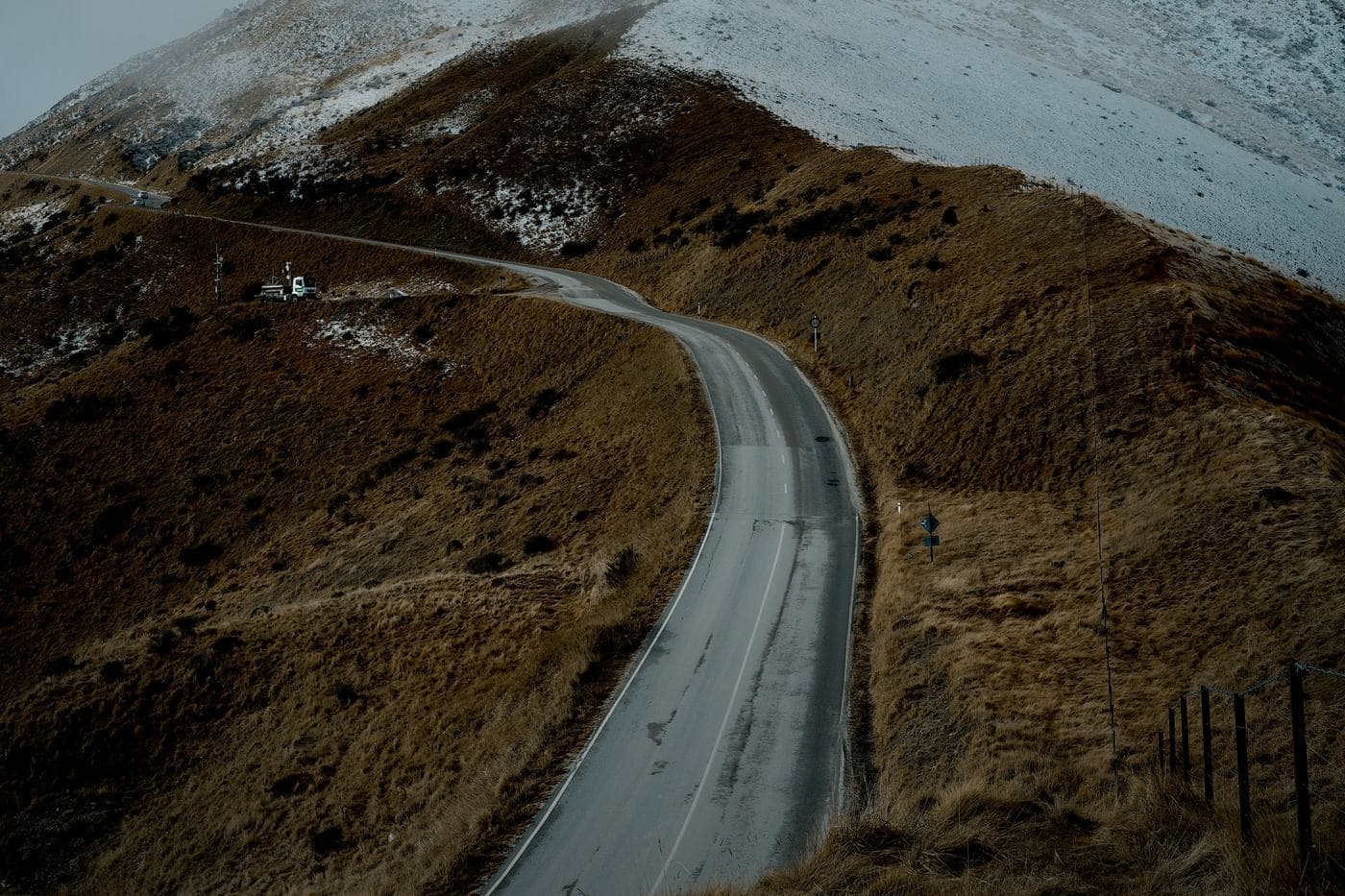 A road winding up a brown tussock hillside into snow and low cloud at The Remarkables, near Queenstown