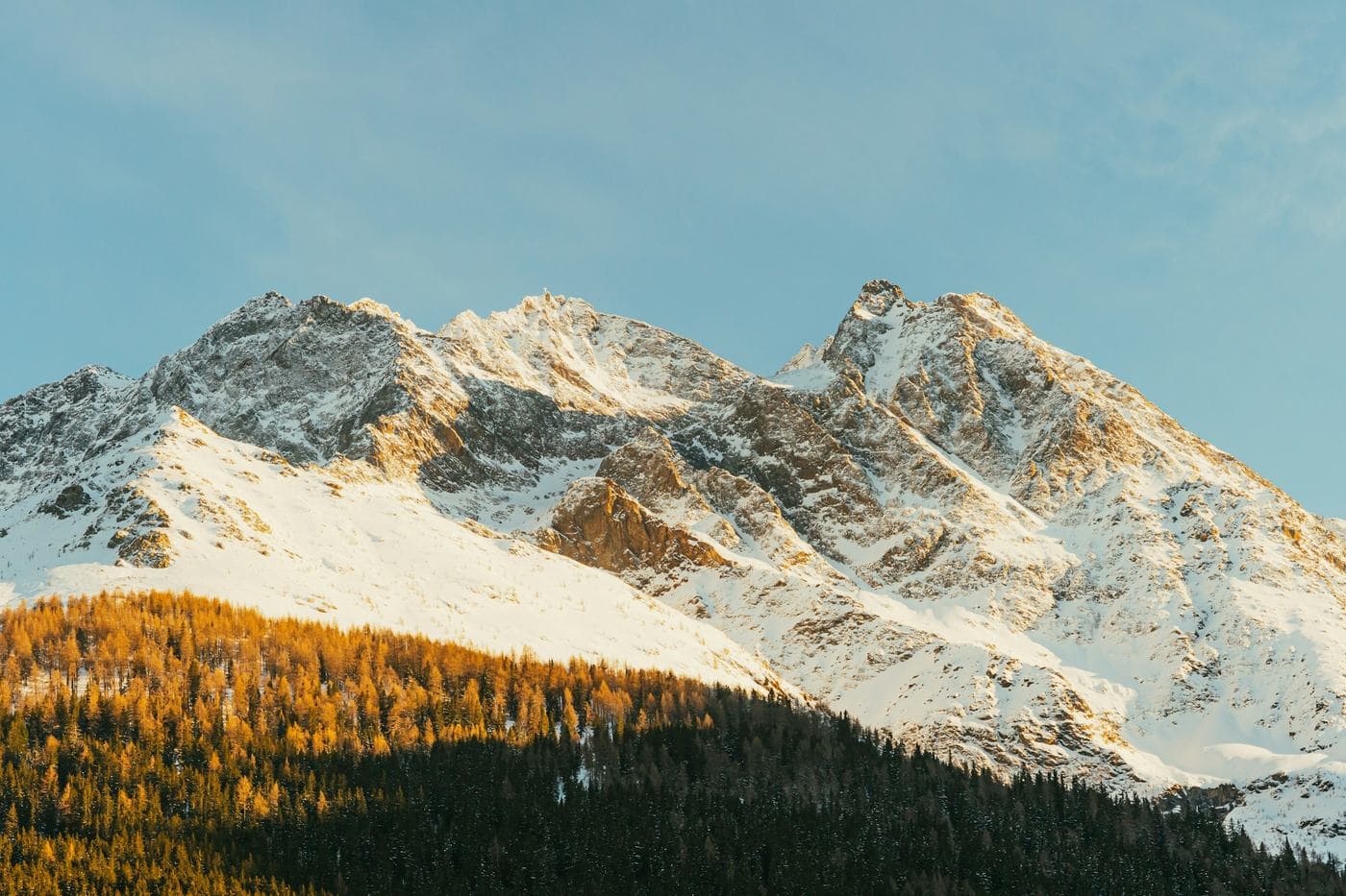 Snow-covered peaks lit gold at the end of the day above a dark forest at St Anton am Arlberg