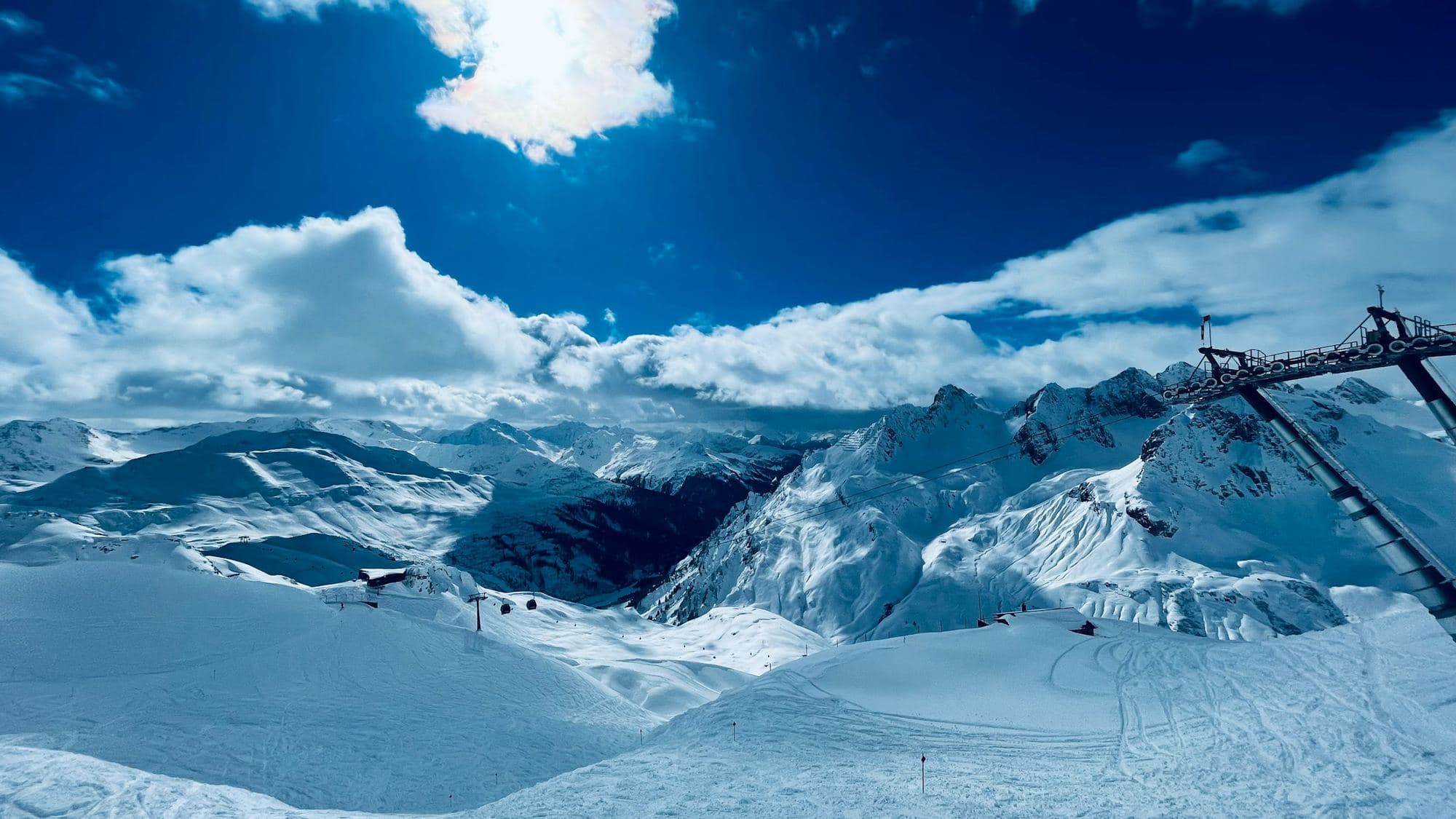 Wide snowy slopes and pistes in the mountains at St Anton am Arlberg, with a lift pylon and a blue sky with clouds