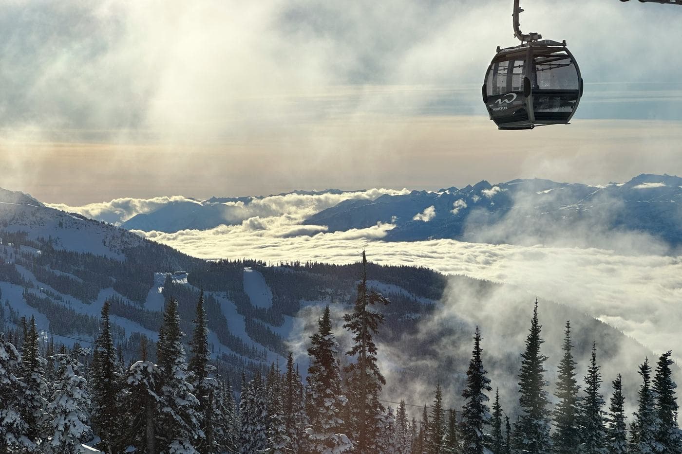A gondola cabin above snowy forest and a sea of cloud, seen from Whistler Blackcomb