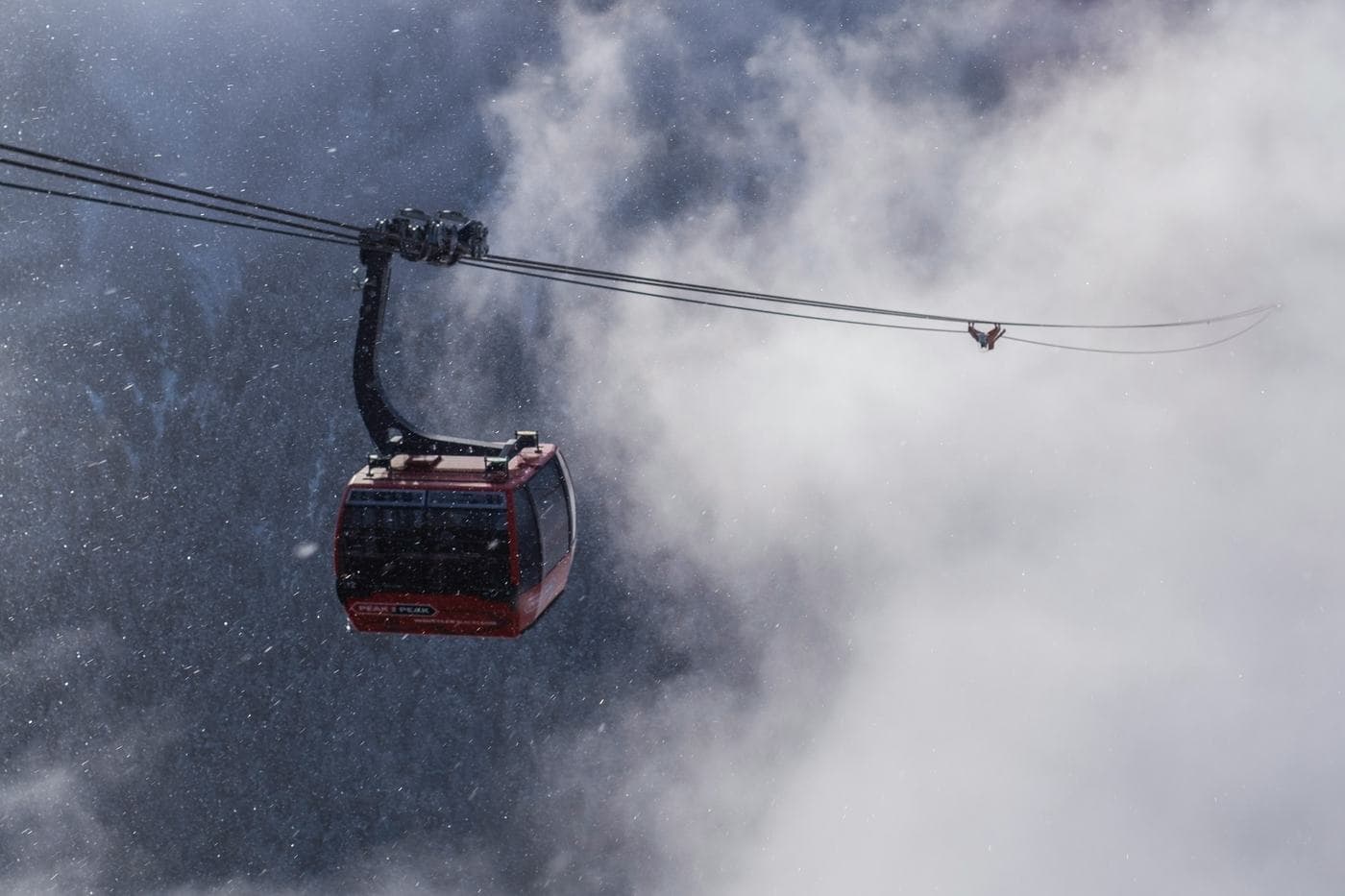 A red gondola cabin crossing through cloud and falling snow above the mountainside at Whistler